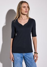 Navyblå v-ringad t-shirt i mjukt material, med korta ärmar och en avslappnad passform, kombinerad med ljustvättade denimjeans och ett gyllene armband.