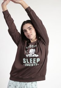 Sudadera marrón de manga larga, con un gráfico de Snoopy y un texto azul claro que dice "SLEEP SOCIETY". Tejido suave, corte holgado.