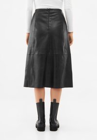 Mustat nahka-midi-hameet, joissa on sileä pinta, paneelidetaljit, takavetoketju ja yhdistetty mustien paksupohjaisten saappaiden kanssa.