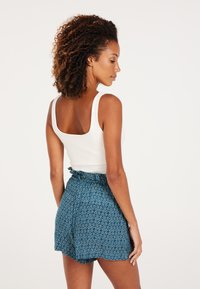 Hvid tanktop med firkantet halsudskæring, parret med mønstrede, blå shorts med en flæse i taljen og subtile abstrakte design.