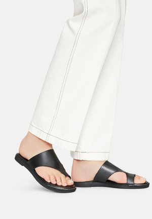 Fekete, sima bőrből készült pánttal ellátott csúszásmentes szandál, széles pántos dizájnnal, nyitott orral és lapos talppal, fehér, széles szárú nadrággal párosítva.