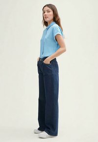 Blusa a righe azzurro chiaro, a maniche corte, abbinata a jeans scuri a vita alta e gamba larga. Scarpe da ginnastica bianche completano il look.