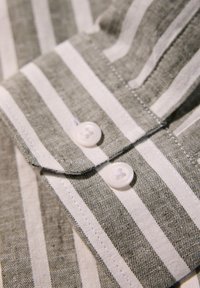 Grønne og hvide stribede stof med linned tekstur, med to hvide knapper med kryds mønster og en spids krave.