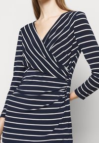 Marinblå klänning med vita horisontella ränder, med en insvängd design, långa ärmar och rynkade detaljer i midjan. Mjuk tygkänsla.