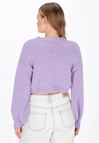 Lila gebreide cropped trui met ribbels aan de mouwen en onderkant, met een gestructureerde afwerking en gezakte schouders, gecombineerd met lichte denim jeans.