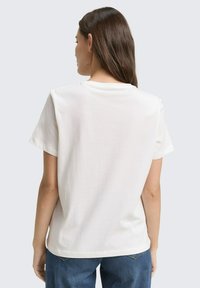 Wit T-shirt met korte mouwen, een losse pasvorm, ronde halslijn en zachte textuur, van achteren getoond. Daaronder worden blauwe jeans gedragen.