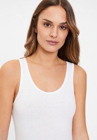Witte tanktop van zacht, lichtgewicht katoen. Heeft een ronde halslijn en brede schouderbanden. Gladde textuur zonder patronen.