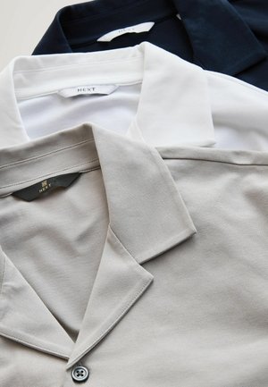 Trois polos en marine, blanc et beige, dotés d'un tissu texturé, de cols classiques et d'étiquettes de logo au niveau du col.