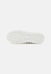 Suela de zapatilla blanca con un patrón texturizado que presenta surcos y crestas profundas para mayor tracción. Hecha de un material de goma duradero.
