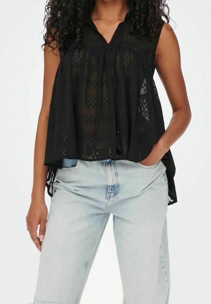 Musta hihaton paita, jossa on laskostettu etuosa, puoliksi läpinäkyvä kangas ja V-pääntie, yhdistettynä vaaleansinihin korkeavyötäröisiin farkkuihin.