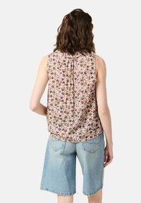 Top sin mangas floral con fondo beige claro, con pequeñas flores multicolores. Combinado con pantalones cortos de mezclilla azul claro.