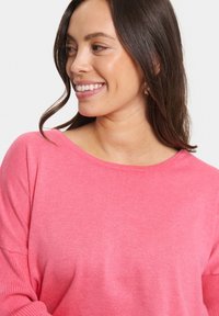 Pull en maille rose clair avec un décolleté large et décontracté et des manches longues. Texture douce sans motifs ni embellissements.