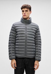 Pelēks padded jaku ar augstu apkakli, pilnu rāvējslēdzēju un dūnu rakstu. Gluda tekstūra ar smalku spīdumu un mazu logotipu uz krūtīm.