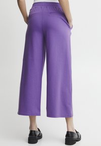 Pantaloni a gamba larga viola realizzati in tessuto morbido, dotati di vita elastica e tasca posteriore. L'orlo è rifinito con una cucitura pulita.