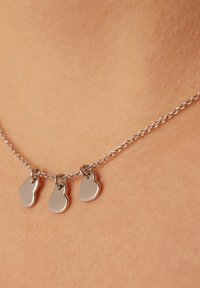 Zilveren ketting met drie kleine, gepolijste hartvormige pendants, die rusten op een gladde huid.