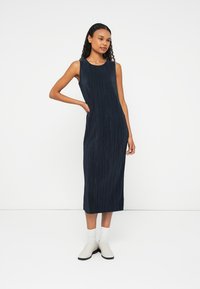 Vestido sem mangas azul-marinho com pregas verticais, até ao joelho, com decote redondo e bolsos laterais. Combinado com botas de tornozelo cinza claro.