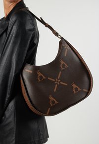 Brown leather shoulder bag with large logo pattern, curved silhouette, and a flat base. Features a smooth texture and an adjustable strap.