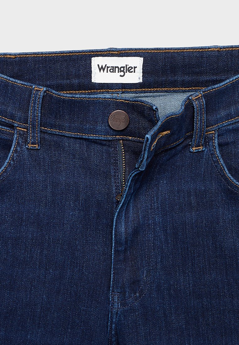 Denim-Jeans von Wrangler in Dunkelblau mit Knopfverschluss, gelben Nähten und einem Etikett am Bund. Klassisches Design mit Reißverschluss.