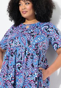 Vestido con estampado paisley en azul, rojo y blanco, con mangas cortas, escote con forma de llave y cintura fruncida. Hecho de tela ligera.