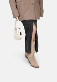 Beige suède enkellaarsjes met puntige neuzen en textuurdetails, gecombineerd met een zwarte spijkerrok met hoge split en een lichtgekleurde handtas.