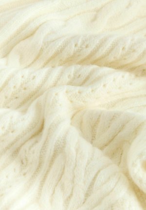 Cable-knit blanket in soft cream wool, featuring textured patterns with raised braids and subtle concentric details throughout.