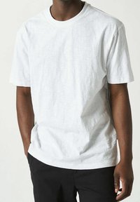Vit kortärmad t-shirt med rund hals, tillverkad av ett strukturerat tyg. Lätt lös passform med diskreta sömnadsdetaljer. Kombinerad med svarta byxor.
