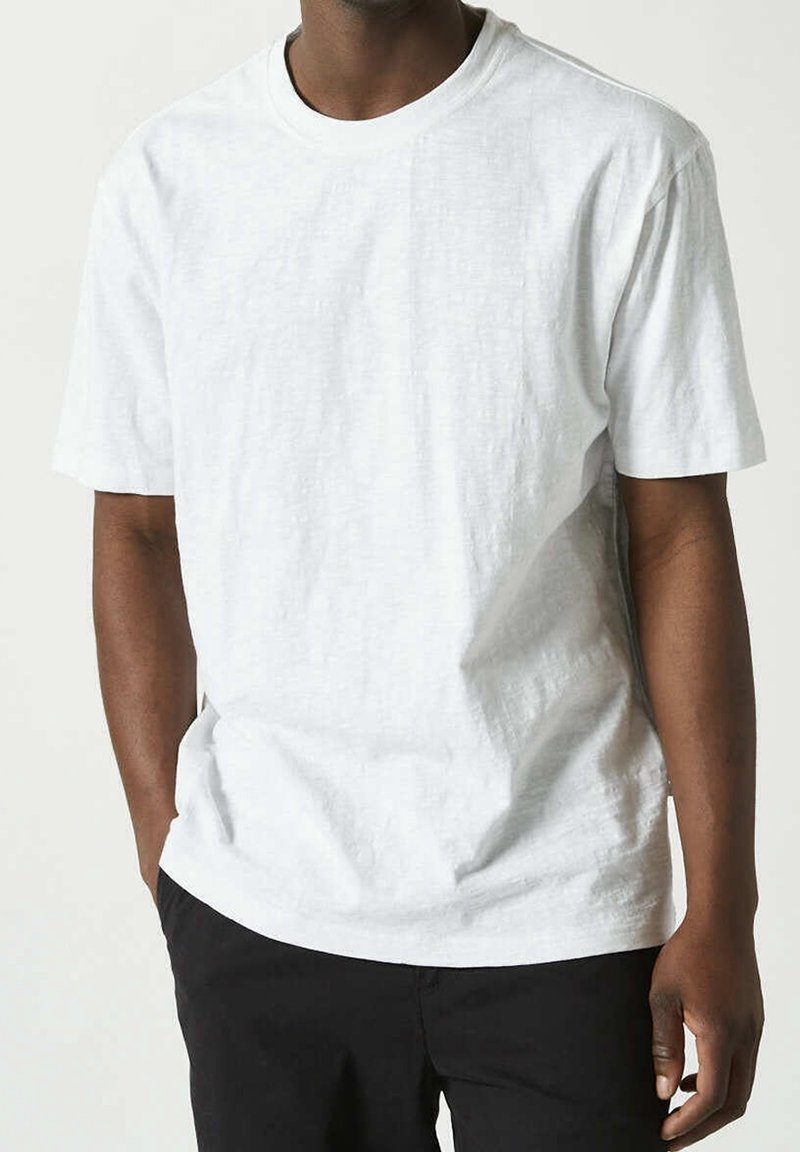 Vit kortärmad t-shirt med rund hals, tillverkad av ett strukturerat tyg. Lätt lös passform med diskreta sömnadsdetaljer. Kombinerad med svarta byxor.
