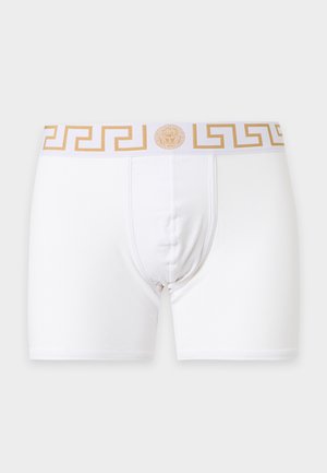 Boxers blancs pour hommes avec un motif clé grec doré et un logo Méduse sur la ceinture, sur fond gris.