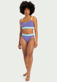 Csíkolt lila bikini szett, amely cropped topból áll, sárga pántokkal és világoskék szalaggal, valamint illeszkedő, állítható derékú alsó résszel.