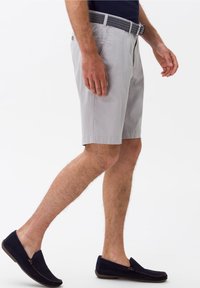 Pantaloni corti grigi chiari con tasche laterali, una texture liscia e una cintura nera a fantasia. Indossati con scarpe slip-on in camoscio blu scuro.