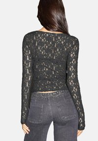 Crna čipkasta majica s dugim rukavima s prilagođenim dizajnom i cvjetnim uzorcima, skraćenog kroja, u kombinaciji s tamnosivim trapericama.
