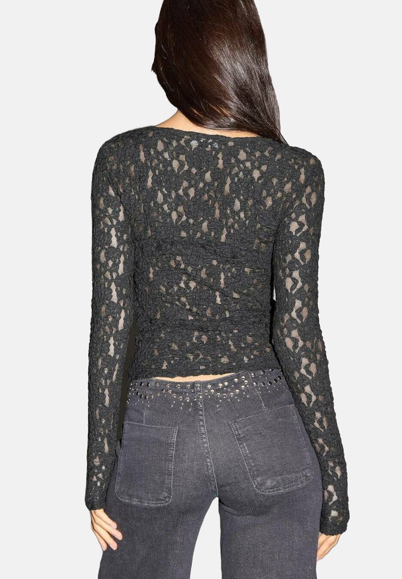 Crna čipkasta majica s dugim rukavima s prilagođenim dizajnom i cvjetnim uzorcima, skraćenog kroja, u kombinaciji s tamnosivim trapericama.