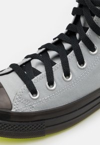 Szare płócienne trampki z czarnymi sznurówkami, srebrnymi oczkami i czubkiem z czarnej gumy. Posiadają teksturowaną czarną podeszwę oraz kontrastujące przeszycia.