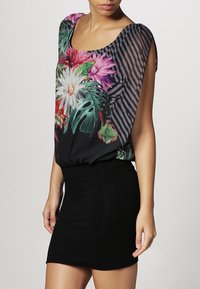 Bluzka w kwiatowy wzór z dopasowaną czarną spódnicą. Góra ma żywe kolory i paski, wykonana jest z lekkiego materiału z elastycznym wykończeniem.