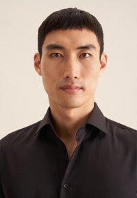 Zwarte overhemddas met een kraag, vervaardigd van een gladde stof, met een gestructureerde pasvorm en een subtiele glans. Geen zichtbare patronen of accenten.