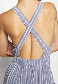 Vêtement sans manches à rayures bleues et blanches, avec des bretelles croisées au dos et une taille élastique. Tissu doux avec une texture légère.