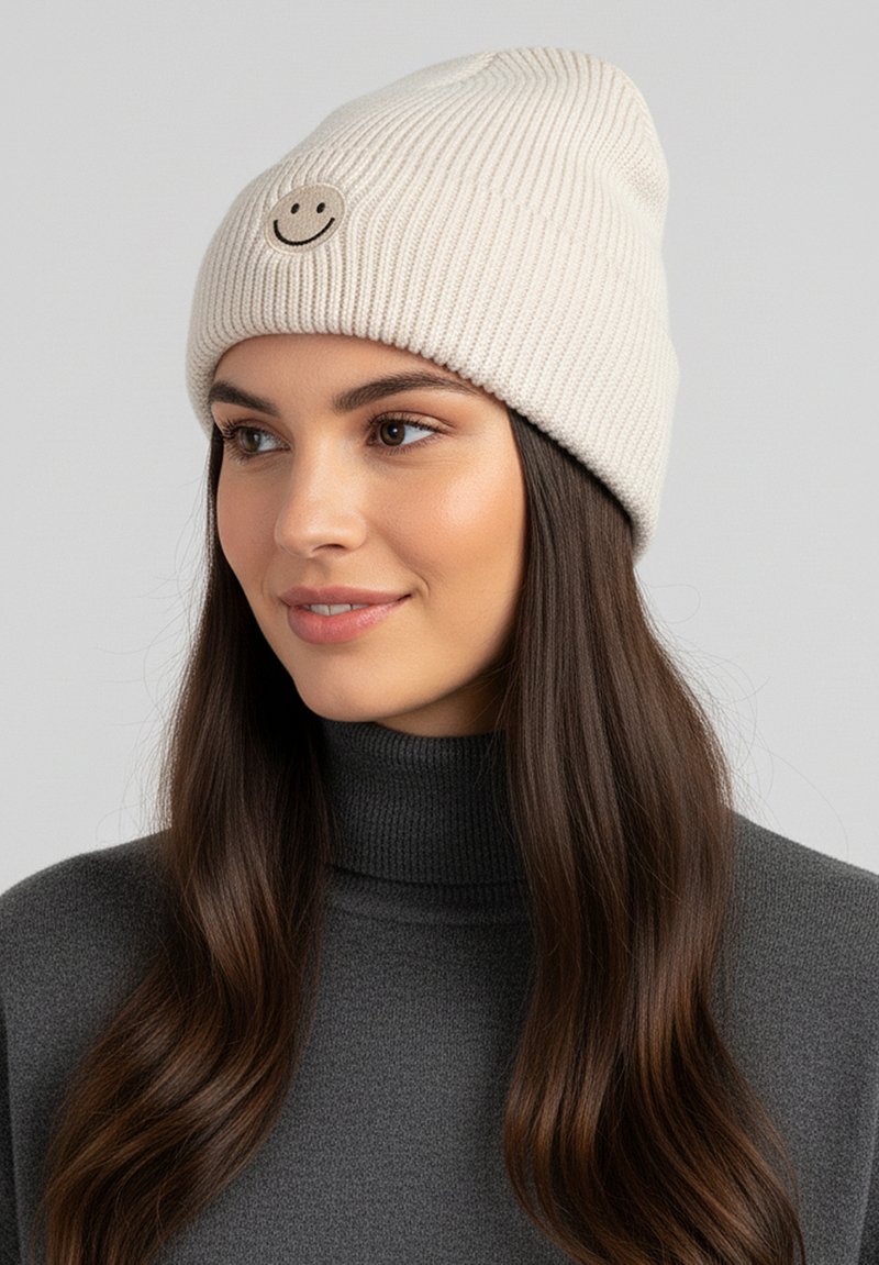 Cream-colored knit beanie with ribbed texture featuring a circular beige patch embossed with a black smiley face.