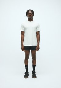 Tricou scurt cu mânecă gri deschis, cu accente negre, purtat cu pantaloni scurți negri, șosete negre și încălțăminte sportivă neagră, stând în fața unui fundal simplu.