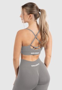 Sujetador deportivo gris con tirantes cruzados en la espalda y detalle de logo. Tejido liso y elástico con un diseño ajustado y leggings de tiro alto a juego.