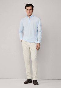 Lichtblauw poloshirt met lange mouwen en kraag, gecombineerd met crèmegekleurde broek en donkerbruine loafers. Eenvoudig en op maat gemaakt ontwerp.