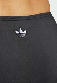 Black athletic shorts with textured fabric; features a small embroidered white Adidas logo at the back. Simple design, elastic waistband.