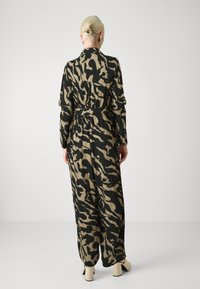 Robe longue et ample en beige avec un imprimé animal abstrait noir, dotée d'une ceinture à la taille et de manches longues. Texture de tissu douce.