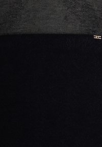 Schwarz und grau gestrickter Stoff, horizontal geteilt; die Oberseite hat eine glatte Textur, die Unterseite ist flauschig mit einem subtilen Glanz. Kleines metallisches Detail enthalten.