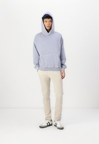 Lyslilla hætte sweatshirt med en frontlomme og justerbar hætte, parret med beige bukser og sorte og hvide kondisko.