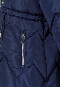 Doudoune bleu marine avec un motif de quilt en diagonale, poche zippée argentée et taille élastiquée pour un look ajusté.