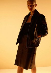 Chaqueta bomber de cuero negro con puños y cuello acanalados, combinada con una falda de cuero negro que presenta una textura suave y un diseño elegante.