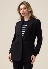 Svart dubbelframmat blazer med snedskurna slag, två framfickor och knappdetaljer. Bärs över en marinblå och vit randig topp.