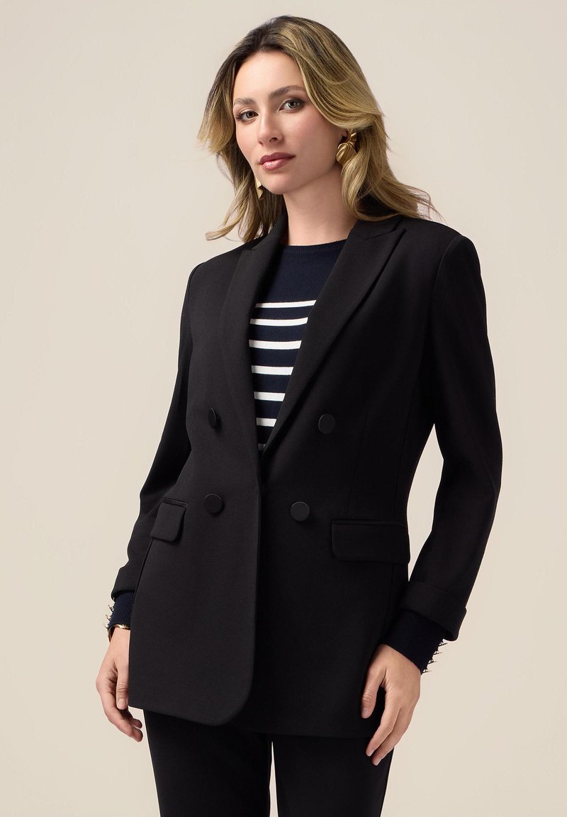 Svart dubbelframmat blazer med snedskurna slag, två framfickor och knappdetaljer. Bärs över en marinblå och vit randig topp.