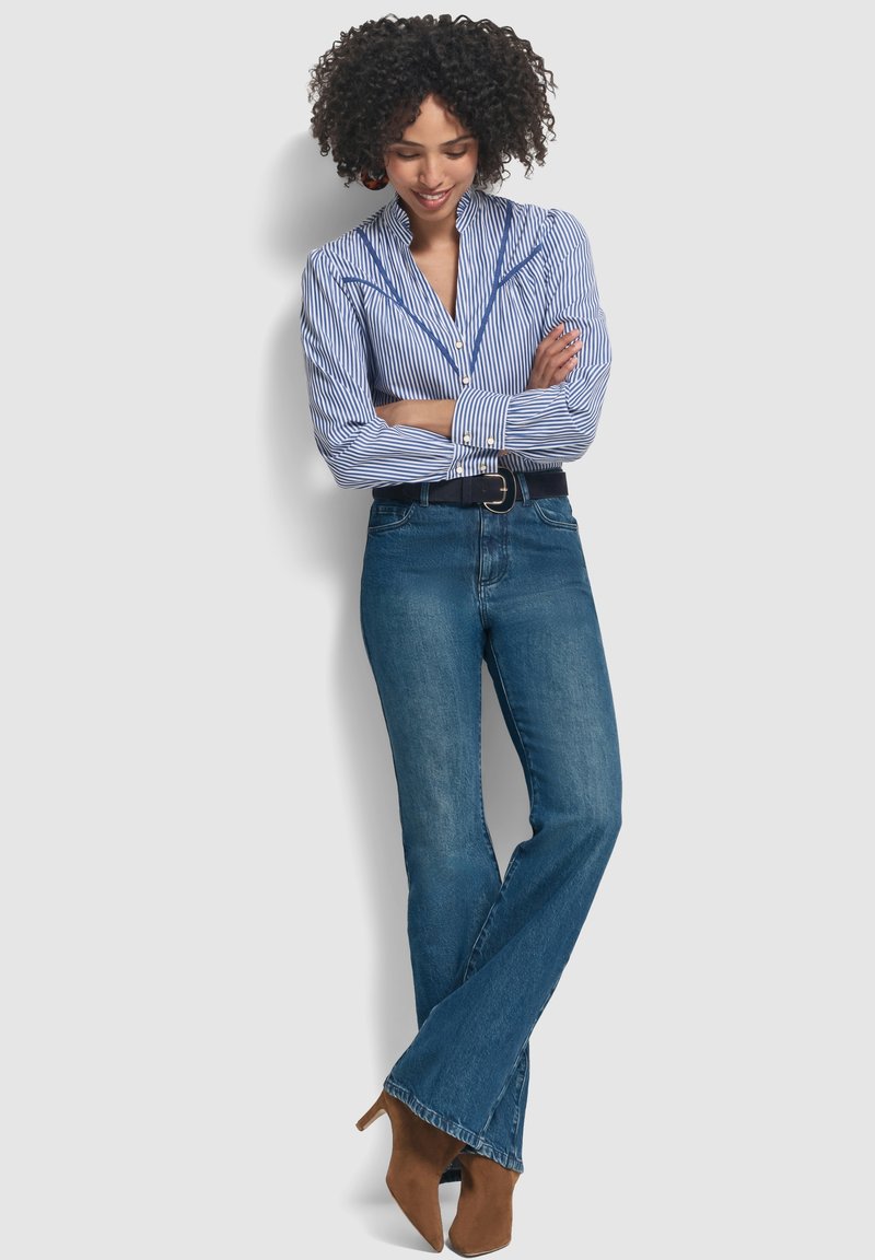 Camicia a righe blu con taglio aderente, abbinata a jeans blu a zampa d'elefante e stivali con tacco marroni, il tutto su uno sfondo neutro.