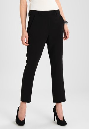 Zwarte op maat gemaakte broek met een rechte snit, gemaakt van een gladde stof, met voorplooien en een klassieke taille. Gemaakt met zwarte hoge hakken.